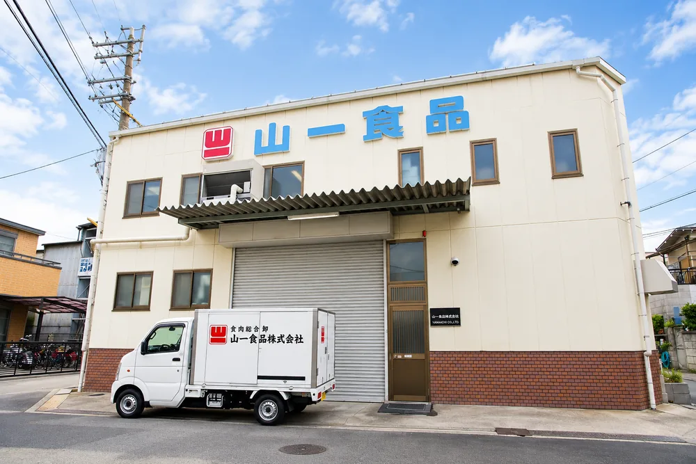 「山一食品」の看板を掲げた加工場の建物と配送車